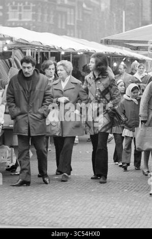 Shopping presso il mercato settimanale, Grote Markt, Haarlem, Grote Markt, The Netherlands Whizgle News, Dutch Desk, The Netherlands, 1950-2000 Una vivace scena di mercato con un gruppo di persone che passeggiano tra varie bancarelle piene di merci. Due donne sono impegnate nella conversazione, mentre uomini e bambini navigano attraverso l'atmosfera vivace, mostrando una miscela di stili e generazioni. Foto Stock
