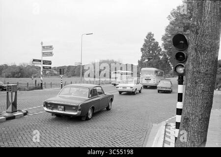 Report NZH Leiden, Noord Zuid Hollandse Vervoersmaatschappij N.V., NZ, 25-10-1971 Whizgle News, Dutch Desk, Paesi Bassi, 1950-2000 Un trafficato incrocio presenta un'auto classica e diversi veicoli che navigano al semaforo, mentre i cartelli stradali indicano varie direzioni in mezzo a uno sfondo di alberi. Foto Stock