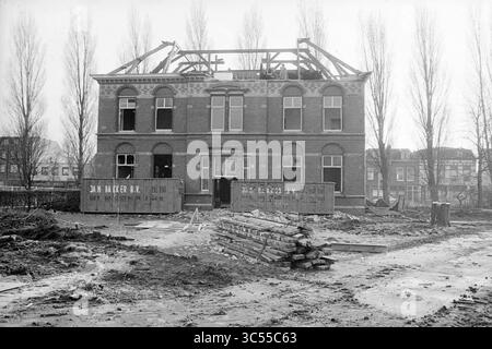 Demolizione, demolizione, demolizione, demolizione, demolizione, scavi, ferrovie, 04-02-1988 Whizgle News, Dutch Desk, Paesi Bassi, 1950-2000 Un edificio parzialmente costruito si erge con un tetto a vista che mostra la sua facciata in mattoni. Intorno alla struttura, i resti di materiali da costruzione sono sparsi per il terreno e alberi alti allineano lo sfondo, aggiungendo contrasto alla scena. La segnaletica sul muro indica il coinvolgimento dell'impresa edile. Foto Stock