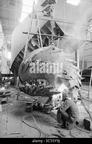 Cantiere Stapel Spaarndam, Spaarndam, Ships, 15-11-1978 Whizgle News, Dutch Desk, i Paesi Bassi, 1950-2000 Anni Un lavoratore salda meticolosamente una grande e complessa componente di macchinari in un ambiente di costruzione, circondato da impalcature e attrezzature pesanti sullo sfondo, mentre dalla torcia di saldatura fuoriesce un pennacchio di fumo. Foto Stock