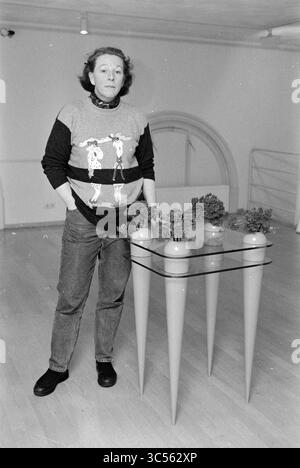 Tre dipendenti del Frans Hals Museum e di Verweyhal, Haarlem, Grote Markt, Paesi Bassi, 05-12-1999 Whizgle News, Dutch Desk, Paesi Bassi, 1950-2000 Una persona si trova accanto a un moderno tavolo di vetro con distintive gambe a forma di cono, adornata con piccole piante. Indossano un maglione con un design grafico divertente e la loro espressione è premurosa quando interagiscono con l'ambiente artistico. Foto Stock