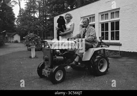 Family Termaat, Families, 23-08-1971 Whizgle News, Dutch Desk, Paesi Bassi, 1950-2000 Una coppia sorridente posa con un piccolo cane, l'uomo seduto su un trattore d'epoca, mentre la donna sta accanto a lui, incorniciata da un incantevole giardino e da una caratteristica casa sullo sfondo. Foto Stock