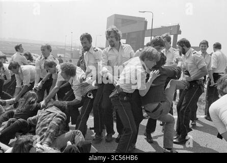 Azione di protesta e blocco della strada contro il trasporto di rifiuti nucleari, IJmuiden, Paesi Bassi, 00-00-1979 Whizgle News, Dutch Desk, i Paesi Bassi, 1950-2000 Un gruppo di individui, tra cui ufficiali in uniforme, sono impegnati in una lotta su strada, con alcune persone sdraiate a terra e altri che tentano di liberarsi. La scena trasmette un senso di conflitto e urgenza, mettendo in evidenza le tensioni tra i gruppi coinvolti. Foto Stock
