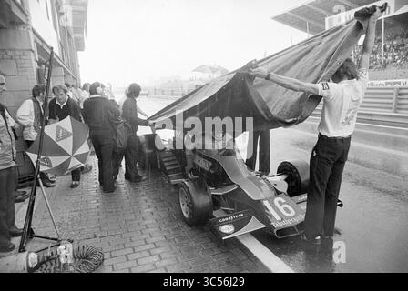 Gare automobilistiche Grand Prix, Grand prix, 27-08-1976 Whizgle News, Dutch Desk, Paesi Bassi, 1950-2000 Una squadra di corse ripara un'auto con un grande telone mentre la pioggia si riversa durante un pit stop, mentre i membri dell'equipaggio e gli spettatori si coprono sotto gli ombrelli. L'atmosfera è tesa, riflettendo le sfide delle corse in condizioni meteorologiche avverse. Foto Stock