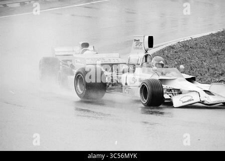 Gara automobilistica sul circuito di Zandvoort con Gijs van Lennep, Zandvoort Whizgle News, Dutch Desk, Paesi Bassi, 1950-2000 due auto da corsa navigano su una pista bagnata, le loro gomme si schiantano tra pozzanghere mentre competono per la posizione in mezzo a una cortina di spruzzi e nebbia. La scena cattura l'intensità e l'emozione degli sport motoristici in condizioni difficili. Foto Stock