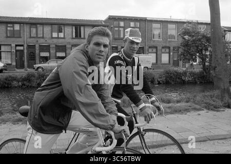 Maertens and Stevenhagen, Cycling, 10-06-1985 Whizgle News, Dutch Desk, Paesi Bassi, 1950-2000 due giovani uomini posano con fiducia sulle loro biciclette, sullo sfondo di edifici pittoreschi e di un canale. Indossano abbigliamento sportivo casual, trasudando un senso di cameratismo e di svago in una giornata nuvolosa. Foto Stock