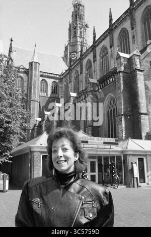 Sig.ra Zifkamp Action Tower Bavo, Haarlem, Leidsevaart, Paesi Bassi, 08-06-1990 Whizgle News, Dutch Desk, Paesi Bassi, 1950-2000 Una donna sorridente si trova di fronte a una grande cattedrale gotica con torreggianti guglie e intricati dettagli architettonici. La scena cattura una miscela di eleganza storica e calore personale, con alberi e un invitante ingresso in primo piano. Foto Stock