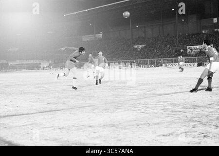 AJAX - Benfica, Football Ajax, 12-02-1969 Whizgle News, Dutch Desk, Paesi Bassi, 1950-2000 Un giocatore salta in testa alla palla in una partita di calcio innevata, mentre compagni di squadra e avversari lo guardano con attenzione in mezzo allo sfondo di una folla affollata sugli spalti. La scena cattura l'intensità e la dinamica del gioco nonostante le difficili condizioni invernali. Foto Stock