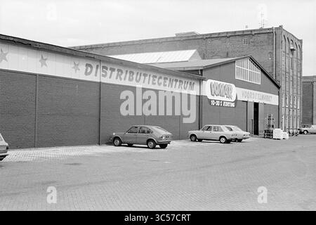 Esterno Vomar porti all'ingrosso IJmuiden, esterno, negozi e chioschi, 20-07-1976 Whizgle News, Dutch Desk, i Paesi Bassi, 1950-2000 Un grande magazzino presenta un cartello per un centro di distribuzione, con auto parcheggiate in primo piano e un edificio adiacente visibile sullo sfondo. L'architettura suggerisce un ambiente industriale tipico delle operazioni commerciali. Foto Stock