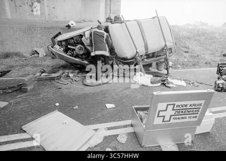 Accident Side Canal - C Road, 28-07-1994 Whizgle News, Dutch Desk, Paesi Bassi, 1950-2000 Una squadra di soccorso lavora diligentemente sulla scena di un veicolo rovesciato, circondato da detriti e attrezzature di emergenza. Un kit di pronto soccorso è esposto in modo prominente, sottolineando la risposta urgente all'incidente. Foto Stock
