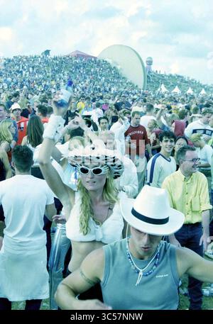 Dance Valley Goers, 03-08-2001 Whizgle News, Dutch Desk, Paesi Bassi, 1950-2000 Una vivace scena di festival all'aperto piena di una folla variegata che si diverte a ballare e ascoltare musica. Una donna con un cappello e occhiali da sole si distingue mentre alza le braccia, mentre gli altri intorno a lei si impegnano in vivaci conversazioni e celebrazioni. L'atmosfera è energica e festosa, con tende lontane e un grande pubblico sullo sfondo. Foto Stock