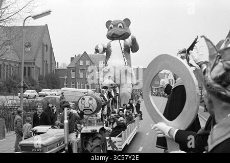 Sfilata di Carnevale, Noordwijkerhout, Carnevale, 07-02-1970 Whizgle News, Dutch Desk, i Paesi Bassi, 1950-2000 Una vivace sfilata presenta una grande e allegra mascotte di orso che conduce un galleggiante. Le persone in costumi vivaci ondeggiano la folla, mentre i bambini e gli adulti apprezzano l'atmosfera festosa. Nelle vicinanze, un trattore tira il galleggiante lungo una strada costeggiata da osservatori ed edifici. Foto Stock