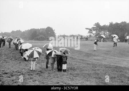 KLM apre varie registrazioni, golf, golf, 29-07-1989','30-07-1989 Whizgle News, Dutch Desk, i Paesi Bassi, 1950-2000 Un gruppo di spettatori si accoccolano sotto ombrelli colorati, osservando attentamente mentre un golfista si prepara a scattare un colpo sotto la pioggia. Il lussureggiante paesaggio verde contrasta con i cieli grigi, catturando un momento di resilienza di fronte alle condizioni meteorologiche avverse. Foto Stock
