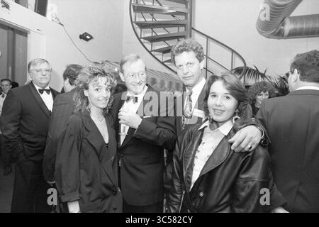 Ricevimento in teatro con Barry Hughes, tra gli altri Whizgle News, Dutch Desk, Paesi Bassi, 1950-2000 Un gruppo di individui elegantemente vestiti socializzano in un evento elegante, con una scala a chiocciola sullo sfondo. Due donne, una con una giacca audace e l'altra con una camicetta classica, stanno in primo piano, mentre gli uomini in smoking si mescolano dietro di loro. L'atmosfera suggerisce un incontro vivace pieno di conversazione e cameratismo. Foto Stock