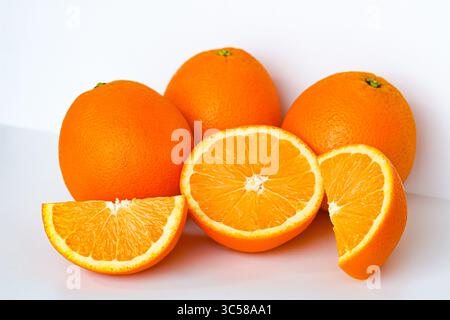 Vivaci arance sunkiste. Tre interi, uno a metà e due fette, catturati con una luce nitida su uno sfondo bianco. Foto Stock