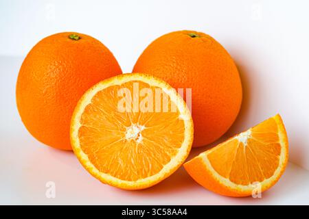 Vivaci arance sunkiste. Due interi, uno a metà e uno a fetta, catturati con una luce nitida su uno sfondo bianco. Foto Stock