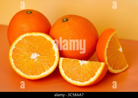 Vivaci arance sunkiste. Due interi, uno a metà e due fette, catturati con una luce nitida su uno sfondo arancione. Foto Stock