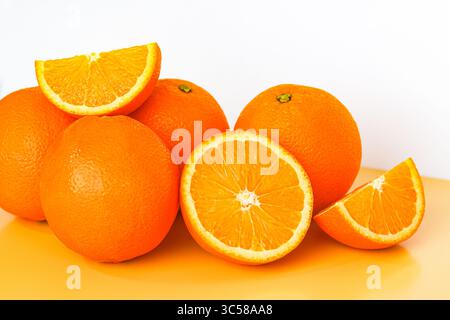 Vivaci arance sunkiste. Quattro interi, uno a metà e due fette, catturati con una luce nitida su uno sfondo arancione e bianco. Foto Stock