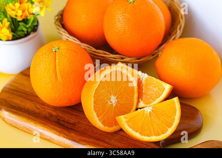 Un gruppo di arance Sunkist intere e affettate disposte su un tagliere di legno e in un cesto, con un piccolo vaso di fiori sullo sfondo. Foto Stock