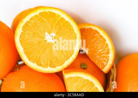 Primo piano di arance mature sunkist, intere e tagliate, immerse in un cestino intrecciato. Un ambiente vivace con frutta. Foto Stock