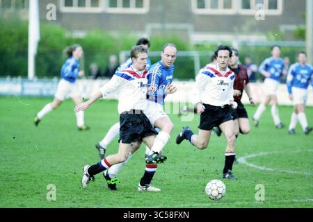 Football Stormvogels-DCG, IJmuiden, Paesi Bassi, 27-04-1998 Whizgle News, Dutch Desk, i Paesi Bassi, 1950-2000 Una partita di calcio dinamica in corso, con giocatori in competizione energica per il pallone. Due atleti in maglie bianche inseguono un giocatore con maglia blu, mentre altri si impegnano nell'azione nelle vicinanze. La scena cattura l'intensità e l'emozione del gioco su un campo erboso. Foto Stock