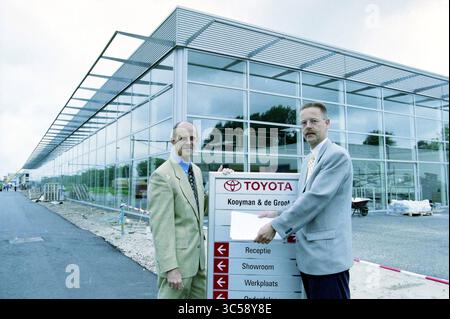 Mr. De Groot e Grijpstra alla Toyota, 07-06-1998 Whizgle News, Dutch Desk, Paesi Bassi, 1950-2000 due uomini in tute formali stanno accanto a un cartello per una concessionaria Toyota, indicando indicazioni come 'reception', 'Showroom' e 'Workplace'. Un moderno edificio con facciata in vetro è visibile sullo sfondo, a indicare la recente costruzione o apertura. Foto Stock