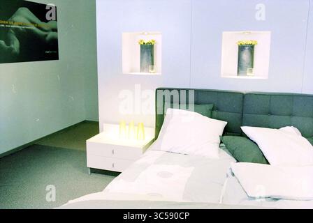 Good Night, Cruquius, Cruquius, 26-09-2001 Whizgle News, Dutch Desk, i Paesi Bassi, 1950-2000 Un'accogliente camera da letto con un letto imbottito grigio con lenzuola bianche e morbidi accenti verdi. L'arredamento minimalista include eleganti lampade da comodino e piccole piante in vaso su scaffali a parete, creando un'atmosfera serena e invitante. Foto Stock