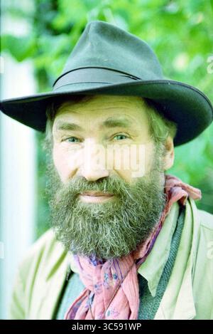 Ritratto di J. Ten Berge, 17-10-1995 Whizgle News, Dutch Desk, Paesi Bassi, 1950-2000 Un uomo con barba piena e un sorriso caldo indossa un cappello a tegole larghe e una sciarpa colorata intorno al collo, trasudando un fascino rustico. I suoi delicati occhi blu trasmettono gentilezza ed esperienza, circondati da uno sfondo verde lussureggiante. Foto Stock