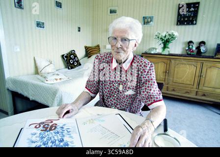 Sig.ra Jansen 95 anni, IJmuiden, IJmuiden, Nederland, 28-07-1998 Whizgle News, Dutch Desk, Paesi Bassi, 1950-2000 una donna anziana con gli occhiali siede a un tavolo, circondata da una camera accogliente decorata con fotografie e decorazioni di famiglia. Guarda attentamente verso il basso un menu floreale mentre una tazza di tè riposa nelle vicinanze. Foto Stock
