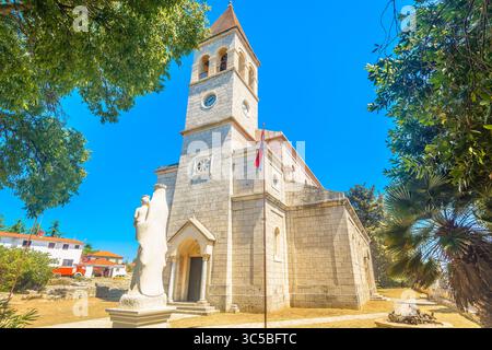 Vista di una storica chiesa in pietra con un alto campanile incastonato tra case rustiche e stradine strette nel tranquillo villaggio di Grohote sulla Solta Foto Stock