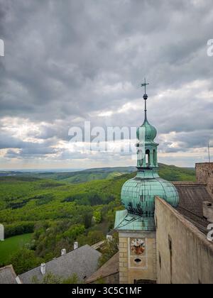 Vista di una torre di rame verde con orologio in cima al castello di Buchlov, che si affaccia su lussureggianti colline boscose sotto un suggestivo cielo nuvoloso. Moravia meridionale, Repubblica Ceca Foto Stock