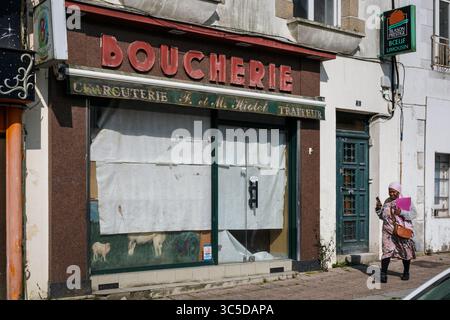 Una donna che passa davanti a una boucherie chiusa a Loudéac, Côtes-d'Armor, Bretagna, Francia Foto Stock