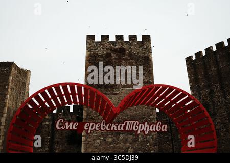 Primo piano della panchina a cuore rosso con iscrizione serba di fronte alla torre della fortezza. Un popolare punto per scattare foto nella fortezza di Smederevo, in Serbia. Foto Stock