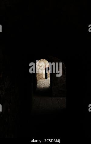 Corridoio scuro all'interno della Fortezza di Smederevo, Serbia, che conduce attraverso porte ad arco fino a muri di pietra illuminati dal sole. Suggestiva architettura medievale. Foto Stock
