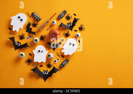 Composizione di Halloween a forma di cuore infestato, pipistrelli, zucche, ragni, oculari e uno scheletro su sfondo giallo. Un posto per il tuo testo, Foto Stock