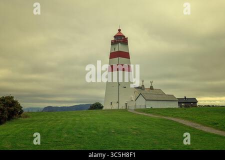 L'iconico faro di Alnes a righe rosse e bianche si erge alto su una collina erbosa sotto un cielo spettacolare in Norvegia. Foto Stock