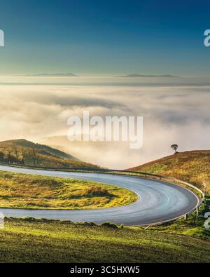 Strada con tornanti nel paesaggio toscano vicino a Volterra in una mattinata nebbiosa. Provincia di Pisa, regione Toscana, Italia Foto Stock