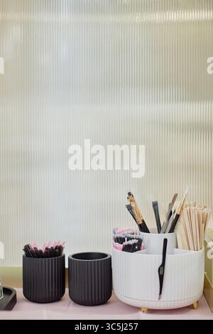 Spazzole per il trucco, bastoncini mascara monouso, bastoncini di cotone e spatole di legno disposti in contenitori neri sul tavolo con spazio per le copie e accesso al salone di bellezza Foto Stock