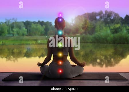 Donna che meditava in Lotus posa in natura, vista posteriore. Sette chakra brillanti Foto Stock
