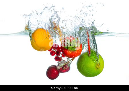 Spruzzi dinamici di frutta fresca assortita, tra cui lime, fragole, ciliegie dolci, albicocche e ribes rosso in acqua limpida, che trasmettono freschezza e vita Foto Stock