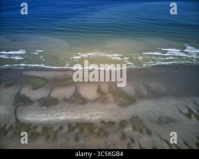 Vista aerea del netto contrasto tra il mare blu profondo e la spiaggia sabbiosa e strutturata che si incontra sulla costa, Dunkerque, Nord, Francia. Foto Stock