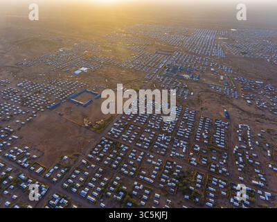 Vista aerea di un vasto insediamento crogiolante sotto la luce del sole dorato, una griglia di strutture in contrasto con il paesaggio arido, Kakuma, Turkana Cou Foto Stock