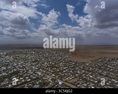 Vista aerea di un fitto insediamento giustapposto al paesaggio arido sotto un vasto cielo, le strutture della città creano un arazzo testurizzato contro i toni della terra, Kakuma, Turkana County, Kenya. Foto Stock