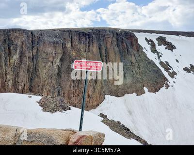 Cartello con il testo "area chiusa - Dangerous Snowfields" di fronte a ripide piste rocciose innevate Foto Stock