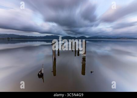 Moody Sunset view sul lago a Torre del Lago Puccini, Toscana, con piloni in legno intemprati da un vecchio molo in primo piano Foto Stock