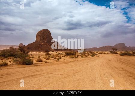 Un'ampia e bassa angolazione cattura una vasta pianura desertica che conduce verso una formazione rocciosa isolata che domina l'orizzonte. Il foregrou sabbioso Foto Stock