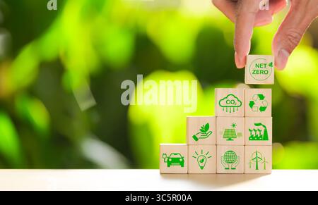 Concetto di impronta di carbonio. Metti a mano un cubo di legno con l'icona della rete zero e l'icona verde sullo sfondo naturale. Zero netto e neutro dal carbonio, emissioni di carbonio, Foto Stock