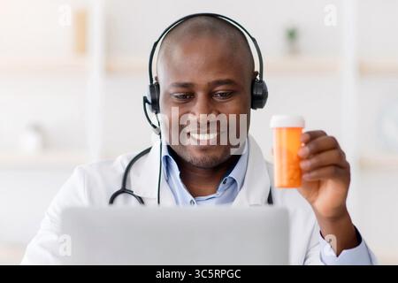 Medico che raccomanda la medicina. Terapeuta afroamericana in cuffie che mostrano il vaso di pillole per lo schermo del computer portatile Foto Stock