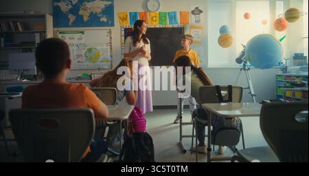 Classe STEM sull'energia rinnovabile: Studente della scuola elementare che parla di fonti di energia davanti alla classe pieno di compagni di classe e insegnanti femminili. Bambini diversi che studiano Ecologia e Scienza. Foto Stock