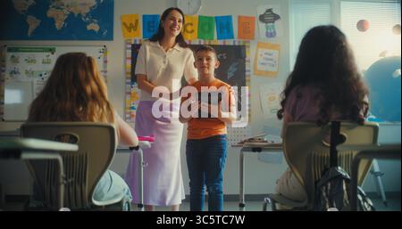 Classe STEM sulle energie rinnovabili: Insegnante donna che presenta una studentessa della scuola elementare. Talented Boy con tablet computer Giving presentazione sull'ecologia davanti all'aula con i compagni di classe. Movimento lento Foto Stock